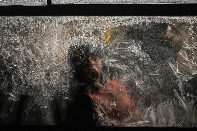 TOPSHOT - A boy tries to remove frost from a frozen window as he rides a bus during a winter evening in Kyiv on January 15, 2026, amid the Russian invasion of Ukraine. (Photo by Sergei GAPON / AFP)