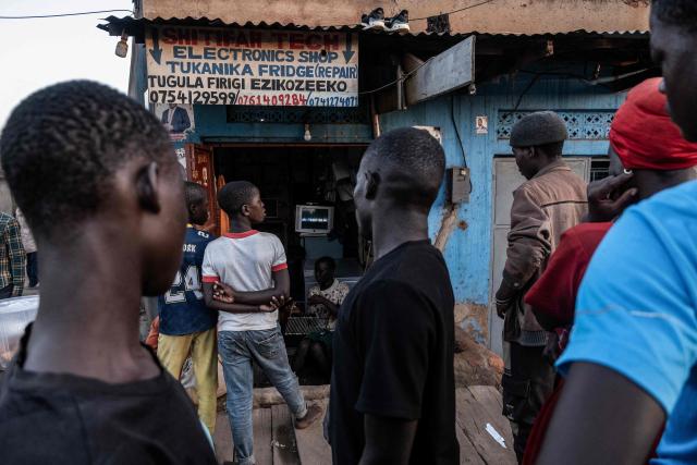 TOPSHOT - People watch a televised broadcast of election updates outside an electronic shop in Kampala on January 15, 2026, during Uganda's 2026 general elections. Polls closed in Uganda on January 15, 2026 after a chaotic day of voting that took place under an internet blackout and with long delays caused by technical breakdowns as President Yoweri Museveni seeks to extend his 40 years in power. Museveni, an 81-year-old who came to power at the head of a rebel army in 1986, is widely expected to win a seventh term in office thanks to his total control of the state and security apparatus. (Photo by Badru Katumba / AFP)