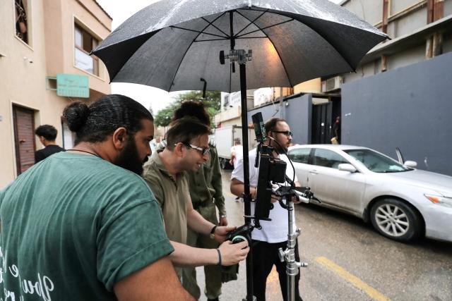Libyan filmmaker Mouayed Zabtia (C) directs his crew as he films outside his home-come-studio, in Tripoli on October 19, 2025. Mouayed Zabtia, 47, shoots most scenes for his latest movie in a studio he built at his Tripoli home. For the filmmaker, it is one way to overcome the obstacles he faces in a country where cinema once nearly vanished. Before a 1969 coup that brought longtime ruler Moamer Kadhafi to power, Libya's capital Tripoli was home to more than 20 movie theatres. Today, Zabtia said, it is no longer censorship that stifles filmmaking in Libya, but an array of other challenges compounded by a lack of public support. (Photo by Mahmud TURKIA / AFP)