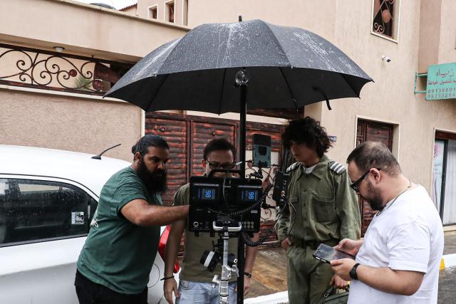 Libyan filmmaker Mouayed Zabtia (C) directs his crew as he films outside his home-come-studio, in Tripoli on October 19, 2025. Mouayed Zabtia, 47, shoots most scenes for his latest movie in a studio he built at his Tripoli home. For the filmmaker, it is one way to overcome the obstacles he faces in a country where cinema once nearly vanished. Before a 1969 coup that brought longtime ruler Moamer Kadhafi to power, Libya's capital Tripoli was home to more than 20 movie theatres. Today, Zabtia said, it is no longer censorship that stifles filmmaking in Libya, but an array of other challenges compounded by a lack of public support. (Photo by Mahmud TURKIA / AFP)