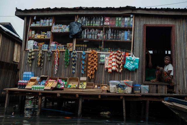 A resident sits in front of a ware shop in Makoko, a floating slum in Lagos, on January 9, 2026. Authorities have demolished hundreds of wooden shacks in Makoko, Africa’s largest and most iconic floating slum, which is built on stilts above the lagoon in the heart of Lagos. The operation is part of an ongoing campaign to remove what officials describe as illegal structures and reclaim waterfront land for modern real-estate developments. (Photo by TOYIN ADEDOKUN / AFP)