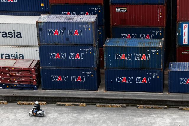 A man rides a scooter past shipping containers at the port in Keelung on January 16, 2026. The United States said on January 15 that it has signed a deal with Taiwan to reduce tariffs on goods from the democratic island, while increasing Taiwanese semiconductor and tech companies' investments in America. (Photo by I-Hwa Cheng / AFP)
