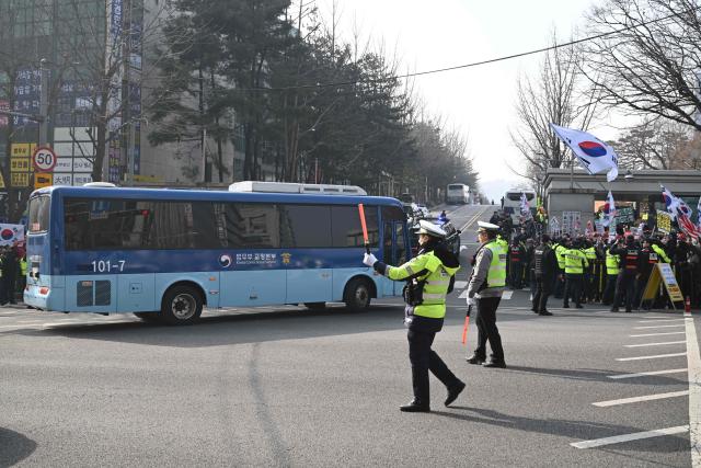 A blue bus believed to be transporting South Korea's impeached former president Yoon Suk Yeol arrives at the Seoul Central District Court in Seoul on January 16, 2026, as his supporters (R) gather in front of the court. A South Korean court will rule on January 16, on whether former president Yoon Suk Yeol obstructed justice during his disastrous martial law declaration and in its chaotic aftermath, the first in a series of verdicts for the disgraced ex-leader. (Photo by Jung Yeon-je / AFP)