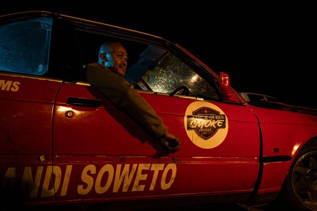 Mojo Mokoena poses for a portrait in his car at the Wheelz’n Smoke Arena in south Johannesburg, on January 15, 2026. Ayanda Mbele and her partner, Monde Hashe, founded the Wheelz’n Smoke Arena to create a safe space for spinners, after a lack of protections at informal spinning spots contributed to the sport’s former illegal status. Once held illegally on Thursday nights, spinning events now continue legally at the Wheelz’n Smoke Arena. (Photo by CAMILLA RICHETTI / AFP)