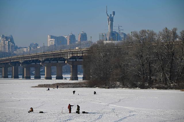 Fishermen fish on the ice-covered Dnieper River as the Motherland Monument appears in the background in Kyiv on January 16, 2026, amid the Russian invasion of Ukraine. (Photo by Sergei GAPON / AFP)