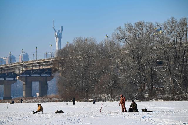 Fishermen fish on the ice-covered Dnieper River as the Motherland Monument appears in the background in Kyiv on January 16, 2026, amid the Russian invasion of Ukraine. (Photo by Sergei GAPON / AFP)