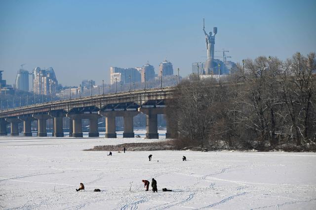 Fishermen fish on the ice-covered Dnieper River as the Motherland Monument appears in the background in Kyiv on January 16, 2026, amid the Russian invasion of Ukraine. (Photo by Sergei GAPON / AFP)