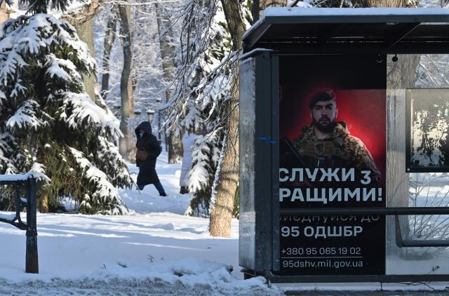 A woman walks behind a bus stop displaying a Ukrainian army recruiting placard during heavy frost in Kyiv on January 16, 2026, amid the Russian invasion of Ukraine. (Photo by Sergei SUPINSKY / AFP)