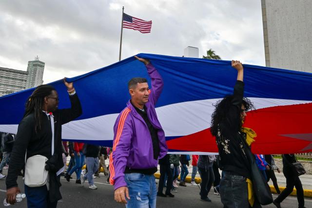 Cubans hold a giant Cuban flag during the US incursion in Venezuela as they take part in the "Anti-Imperialist" protest in front of the US Embassy in Havana on January 16, 2026. The capture by US forces of Venezuelan leader Nicolas Maduro on January 3, 2026, and the killing in the operation of 32 Cubans assigned to protect him represent a major blow for the island's revered intelligence services, experts say. (Photo by ADALBERTO ROQUE / AFP)