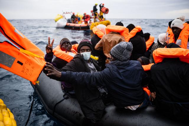 Migrants onboard a rubber boat receive life jackets as crew members of the “Ocean Viking” rescue ship carry out a rescue operation using a RHIB (Rigid inflatable boat) in the search-and-rescue zone off the international waters of Libya, on January 16, 2026. 46 migrants on a rubber dinghy in distress were rescued by the crew of the "Ocean Viking" in international waters off the coast of Libya as they attempted to reach the shores of the Italian island of Lampedusa. Libya, located about 300 km from the Italian coast, is one of the main departure points in North Africa for migrants, mostly from sub-Saharan Africa, risking their lives attempting to cross the Mediterranean sea. This is the first rescue of the year carried out by the ship operated by the NGO SOS Mediterranee. (Photo by Sameer Al-DOUMY / AFP)