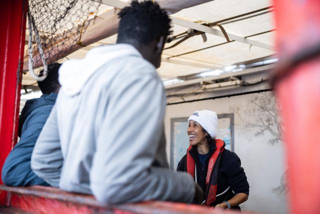 A crew member of the “Ocean Viking” rescue ship distributes bracelets to migrants onboard the “Ocean Viking” rescue ship after they were rescued in the search-and-rescue zone off the international waters of Libya, on January 16, 2026. 46 migrants on a rubber dinghy in distress were rescued by the crew of the "Ocean Viking" in international waters off the coast of Libya as they attempted to reach the shores of the Italian island of Lampedusa. Libya, located about 300 km from the Italian coast, is one of the main departure points in North Africa for migrants, mostly from sub-Saharan Africa, risking their lives attempting to cross the Mediterranean sea. This is the first rescue of the year carried out by the ship operated by the NGO SOS Mediterranee. (Photo by Sameer Al-DOUMY / AFP)