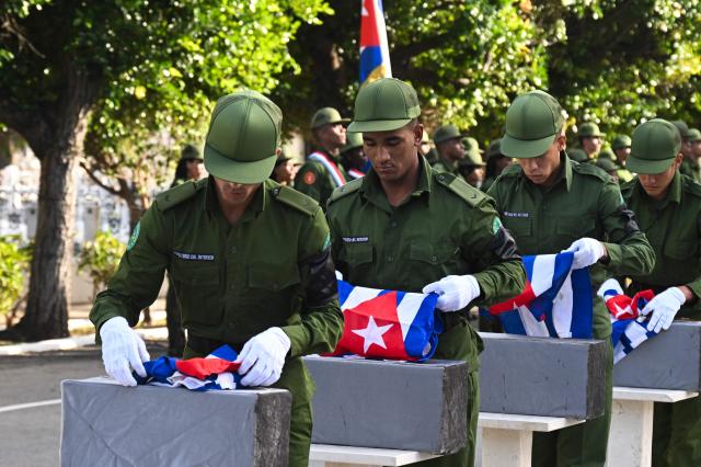 Cuban soldiers place Cuban flags on top of the remains of some of the 32 Cuban soldiers killed during the US incursion in Venezuela during their funeral at Colon cemetery in Havana on January 16, 2026. The capture by US forces of Venezuelan leader Nicolas Maduro on January 3, 2026, and the killing in the operation of 32 Cubans assigned to protect him represent a major blow for the island's revered intelligence services, experts say. (Photo by ADALBERTO ROQUE / AFP)