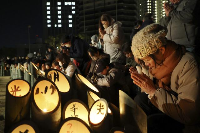 People pray for victims around candles commemorating the 31st anniversary of the "Great Hanshin Earthquake" at a park in Kobe, Hyogo prefecture on January 17, 2026. The port city of Kobe was hit by a 7.2 magnitude quake on January 17, 1995, killing 6,434 people and levelling much of the city. (Photo by JIJI PRESS / AFP) / Japan OUT