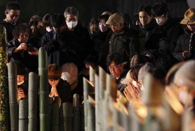People pray for victims around candles commemorating the 31st anniversary of the Great Hanshin Earthquake at a park in Kobe, Hyogo prefecture on January 17, 2026. The port city of Kobe was hit by a 7.2 magnitude quake on January 17, 1995, killing 6,434 people and levelling much of the city. (Photo by JIJI PRESS / AFP) / Japan OUT