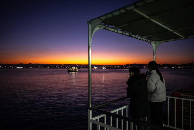 Passengers take in the view from the deck of a ferry sailing from Sakurajima port to Kagoshima city at dusk on January 16, 2026. (Photo by Philip FONG / AFP)