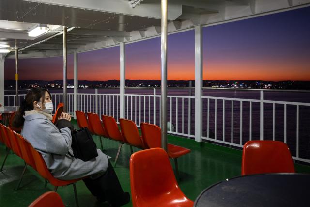 A passenger takes in the view while sitting on the deck of a ferry sailing from Sakurajima port to Kagoshima city at dusk on January 16, 2026. (Photo by Philip FONG / AFP)