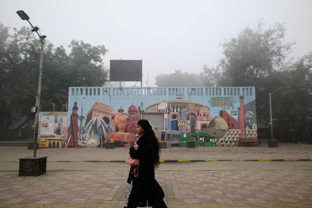 A woman walks past a mural amid dense fog in New Delhi on January 17, 2026. (Photo by Manan VATSYAYANA / AFP)