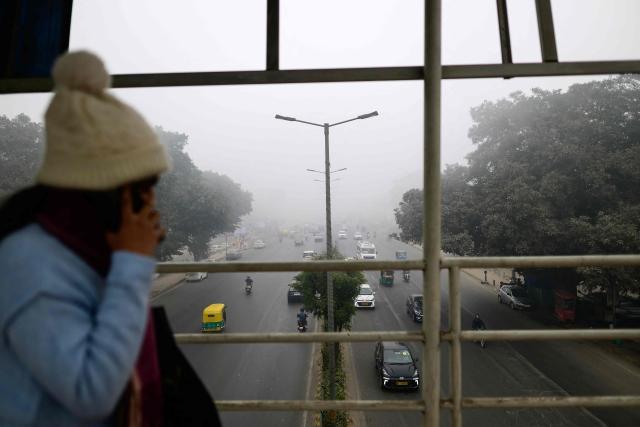 A woman walks on a foot-over-bridge amid dense fog in New Delhi on January 17, 2026. (Photo by Manan VATSYAYANA / AFP)