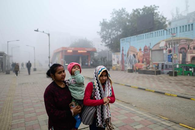 A family walks along a street amid dense fog in New Delhi on January 17, 2026. (Photo by Manan VATSYAYANA / AFP)