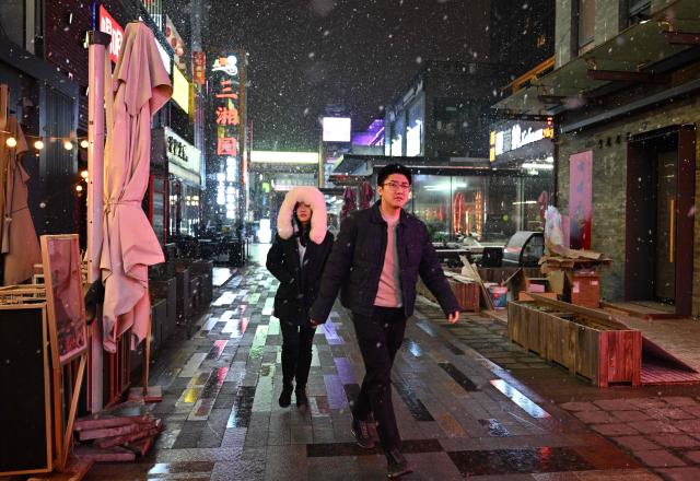 People walk past restaurants during snow fall in Beijing on January 17, 2026. (Photo by ADEK BERRY / AFP)