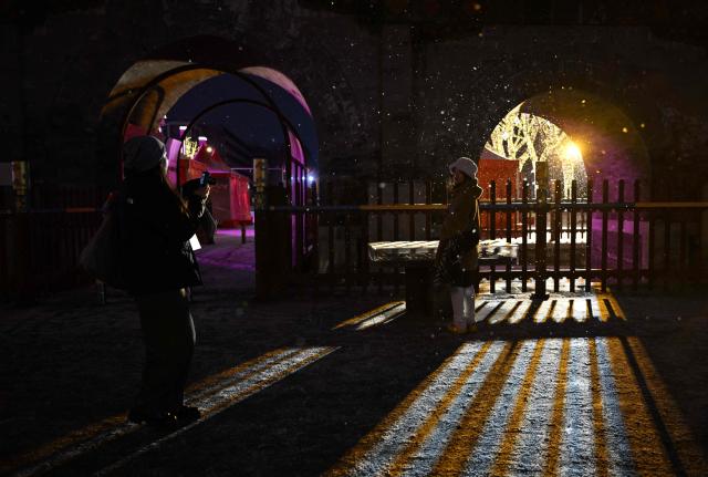 A woman (L) takes pictures of her friend during snow fall in Beijing on January 17, 2026. (Photo by ADEK BERRY / AFP)