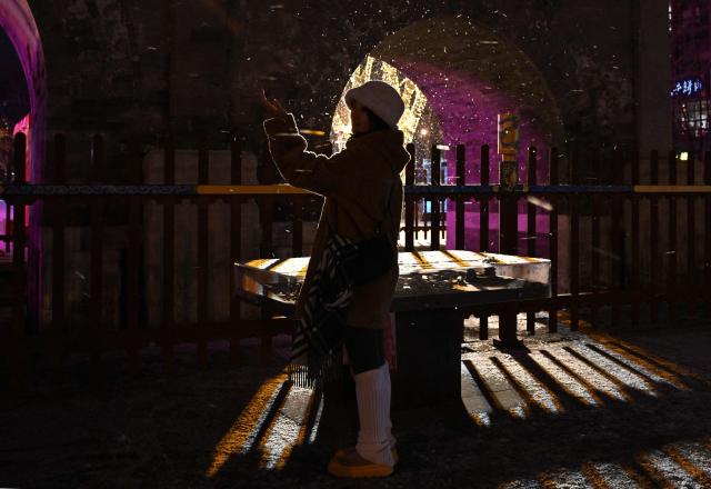 A woman poses for pictures during snow fall in Beijing on January 17, 2026. (Photo by ADEK BERRY / AFP)