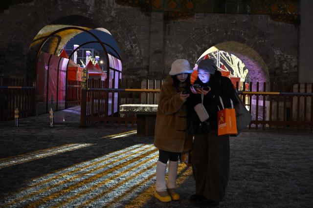 Women check their phones during snow fall in Beijing on January 17, 2026. (Photo by ADEK BERRY / AFP)