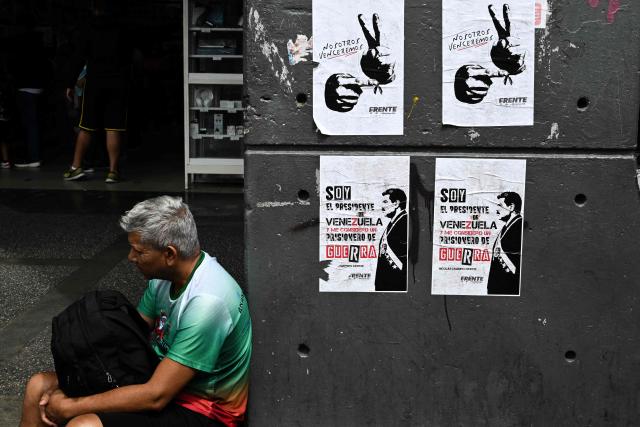 A man sits next to signs supporting ousted Venezuelan President Nicolas Maduro in Caracas on January 17, 2026. (Photo by Ronaldo SCHEMIDT / AFP)
