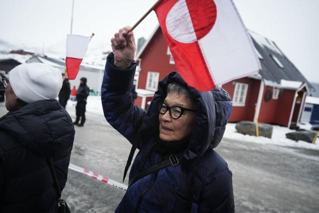 A woman with the Greenlandic flag is seen as people take part in a demonstration that gathered almost a third of the city population to protest against the US President's plans to take Greenland, on January 17, 2026 in Nuuk, Greenland, in front of the US Consulate to Greenland. US President Donald Trump escalated his quest to acquire Greenland, threatening multiple European nations with tariffs of up to 25 percent until his purchase of the Danish territory is achieved. Trump's threats came as thousands of people protested in the capital of Greenland against his wish to acquire the mineral-rich island at the gateway to the Arctic. (Photo by Alessandro RAMPAZZO / AFP)
