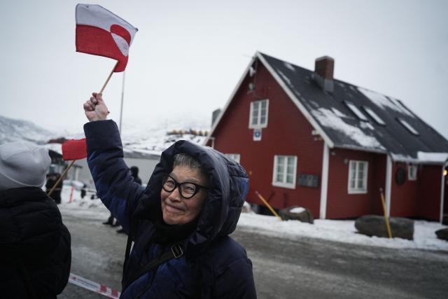 A woman with the Greenlandic flag is seen as people take part in a demonstration that gathered almost a third of the city population to protest against the US President's plans to take Greenland, on January 17, 2026 in Nuuk, Greenland, in front of the US Consulate to Greenland. US President Donald Trump escalated his quest to acquire Greenland, threatening multiple European nations with tariffs of up to 25 percent until his purchase of the Danish territory is achieved. Trump's threats came as thousands of people protested in the capital of Greenland against his wish to acquire the mineral-rich island at the gateway to the Arctic. (Photo by Alessandro RAMPAZZO / AFP)