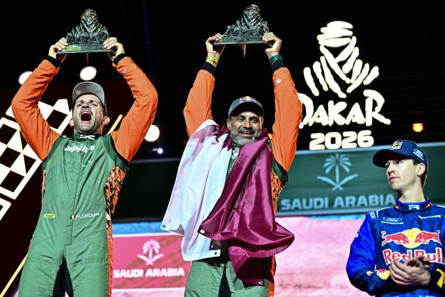 The Dacia Sandriders' Qatari driver Nasser al-Attiyah (R) and Belgian copilot Fabian Lurquin lift the winner's trophy as they celebrate on the podium after winning the 48th edition of the Dakar Rally 2026 in Yanbu, Saudi Arabia, on January 17, 2026. Qatar's Nasser Al-Attiyah secured his sixth Dakar Rally car title in Saudi Arabia. (Photo by Giuseppe CACACE / AFP)