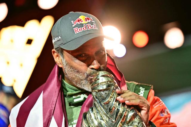 The Dacia Sandriders' Qatari driver Nasser al-Attiyah kisses the winner's trophy as he and his teammate celebrate on the podium after winning the 48th edition of the Dakar Rally 2026 in Yanbu, Saudi Arabia, on January 17, 2026. Qatar's Nasser Al-Attiyah secured his sixth Dakar Rally car title in Saudi Arabia. (Photo by Giuseppe CACACE / AFP)