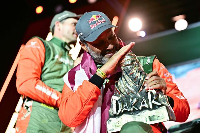 The Dacia Sandriders' Qatari driver Nasser al-Attiyah reacts with the winner's trophy as he and his teammate celebrate on the podium after winning the 48th edition of the Dakar Rally 2026 in Yanbu, Saudi Arabia, on January 17, 2026. Qatar's Nasser Al-Attiyah secured his sixth Dakar Rally car title in Saudi Arabia. (Photo by Giuseppe CACACE / AFP)
