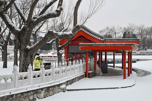 People take pictures as they visit the Beihai Park amid snowfall in Beijing on January 18, 2026. (Photo by ADEK BERRY / AFP)