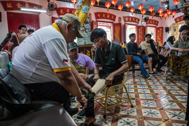 A volunteer fits a prosthetic leg for a teenager, as part of a social service event distributing prosthetics for free to people with physical disabilities organised by a Chinese foundation, at the Boen Bio Temple in Surabaya on January 18, 2026. (Photo by Juni KRISWANTO / AFP)