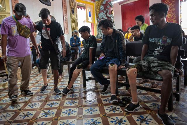 A man (2nd L) tries to walk after being fitted with a prosthetic leg, distributed for free to people with physical disabilities as part of a social service event by a Chinese foundation, at the Boen Bio Temple in Surabaya on January 18, 2026. (Photo by Juni KRISWANTO / AFP)