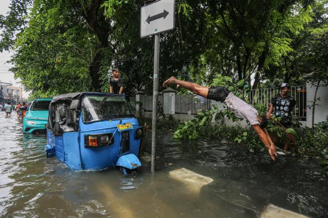 TOPSHOT - A youth dives into floodwaters after heavy rain left residential areas partially submerged in Jakarta on January 18, 2026. (Photo by AFP)