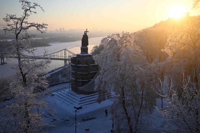 A pedestrian walks their dog past the Volodymyr The Great Monument as sun rises and the temperature dropped to -15 degrees Celsius in Kyiv on January 18, 2026, amid the Russian invasion of Ukraine. (Photo by Sergei GAPON / AFP)