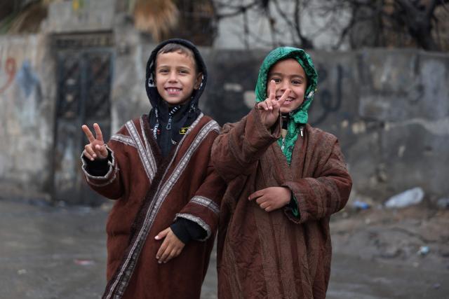 Children gesture while standing along a street in Tabqa, in Raqa province, on the southwestern banks of the Euphrates on January 18, 2026. Kurdish-led forces withdrew on January 18 from Syria's largest oil field, a conflict monitor said, as government troops extended their grip over swathes of territory in the country's north and east. Government troops drove Kurdish forces from two Aleppo neighbourhoods following clashes last week, and on January 17 announced they had captured an area east of the city, as well as Tabqa. (Photo by OMAR HAJ KADOUR / AFP)