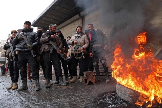 Syrian government troops stand guard next to a burning tyre along a street of Tabqa, in Raqa province, on the southwestern banks of the Euphrates on January 18, 2026. Kurdish-led forces withdrew on January 18 from Syria's largest oil field, a conflict monitor said, as government troops extended their grip over swathes of territory in the country's north and east. Government troops drove Kurdish forces from two Aleppo neighbourhoods following clashes last week, and on January 17 announced they had captured an area east of the city, as well as Tabqa. (Photo by OMAR HAJ KADOUR / AFP)