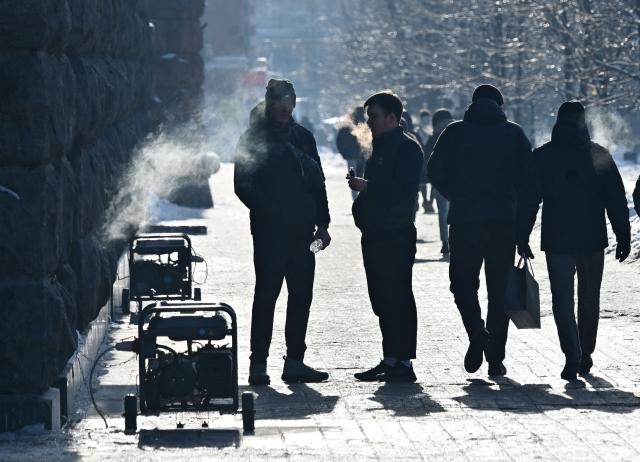 Pedestrians walk past running power generators in the centre of Kyiv during heavy frost on January 18, 2026, amid the Russian invasion of Ukraine. Russian attacks have left Ukraine's energy grid teetering on the brink of collapse and have disrupted power and water supplies to millions over recent weeks. (Photo by Sergei SUPINSKY / AFP)