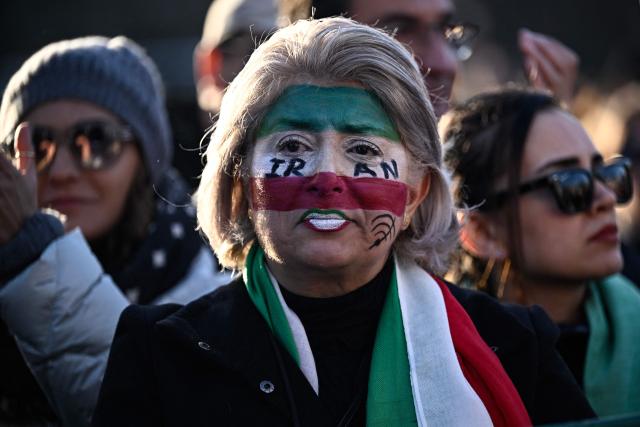 A protester wearing facepaint in Iranian national colours looks on during the March for Iran rally in support of the Iranian people, called by pro-royalists and supporters of the son of the last shah of Iran Mohammad Reza Pahlavi at the Place Victor Hugo, in Paris on January 18, 2026. (Photo by JULIEN DE ROSA / AFP)