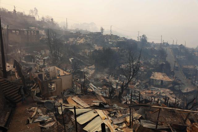 A resident walks amid the charred remains of destroyed homes after a wildfire in Concepcion, Chile, on January 18, 2026. Wildfires raging in southern Chile have killed at least 15 people and forced more than 50,000 to evacuate, the government said. (Photo by Raul BRAVO / AFP)