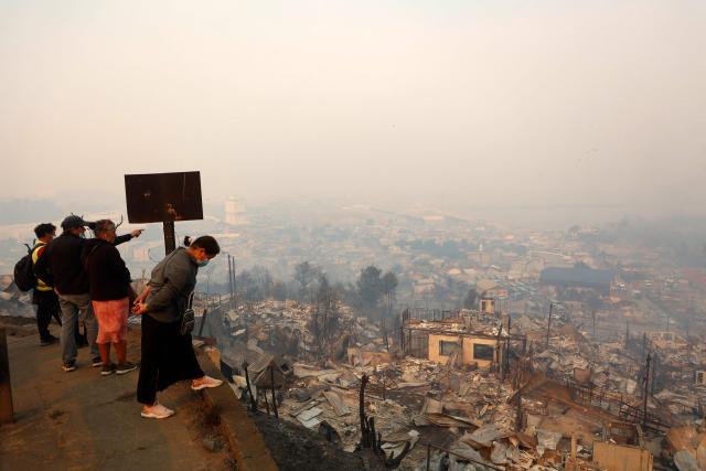 Residents look at burned houses after a wildfire in Concepcion, Chile, on January 18, 2026. Wildfires raging in southern Chile have killed at least 15 people and forced more than 50,000 to evacuate, the government said. (Photo by Raul BRAVO / AFP)