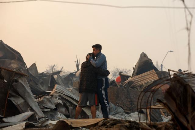 Residents comfort each other amid burned houses after a wildfire in Concepcion, Chile, on January 18, 2026. Wildfires raging in southern Chile have killed at least 15 people and forced more than 50,000 to evacuate, the government said. (Photo by Raul BRAVO / AFP)
