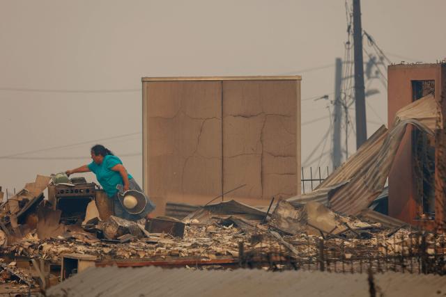 A resident tries to rescue belongings from the charred remains of her destroyed home after a wildfire in Concepcion, Chile, on January 18, 2026. Wildfires raging in southern Chile have killed at least 15 people and forced more than 50,000 to evacuate, the government said. (Photo by Raul BRAVO / AFP)