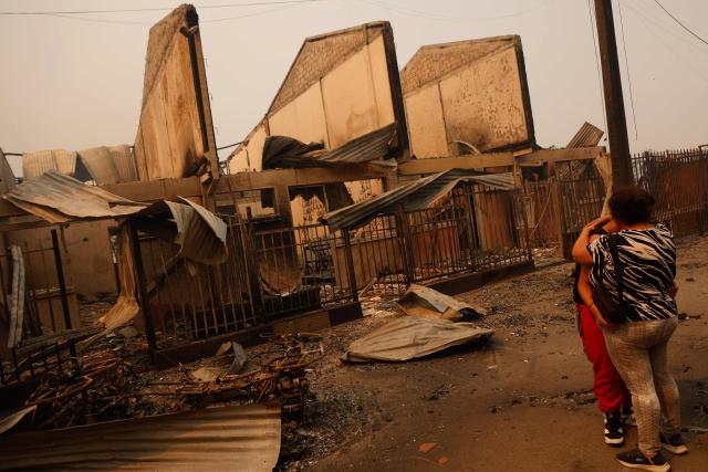 Residents comfort each other in front of burned houses after a wildfire in Concepcion, Chile, on January 18, 2026. Wildfires raging in southern Chile have killed at least 15 people and forced more than 50,000 to evacuate, the government said. (Photo by Raul BRAVO / AFP)