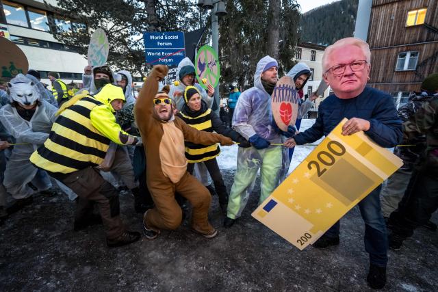A protester wearing a mask of Rheinmetall CEO Armin Papperger holds a cardboard cut-out euro banknote during a demonstration against the World Economic Forum (WEF) on the eve of the WEF annual meeting in Davos on January 18, 2026. (Photo by Fabrice COFFRINI / AFP)