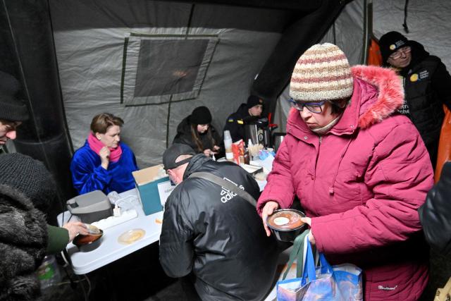 People have a meal in a tent, one of "Points of Invincibility", organized for residents to warm themselves and charge their electronic devices during blackout and heavy frost in Kyiv on January 18, 2026, amid Russian invasion in Ukraine. Russian attacks have left Ukraine's energy grid teetering on the brink of collapse and have disrupted power and water supplies to millions over recent weeks. (Photo by Sergei SUPINSKY / AFP)