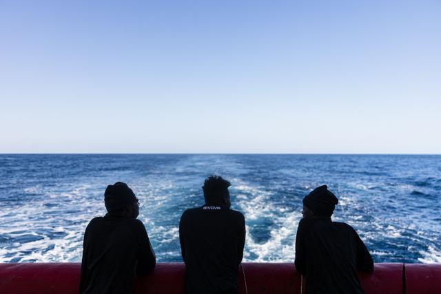Migrant sit on the aft deck of the rescue ship "Ocean Viking" operated by the NGO SOS Mediterranee, as it sails toward a distress case in the search-and-rescue zone in international waters off the coast of Libya, on January 17, 2026. (Photo by Sameer Al-DOUMY / AFP)